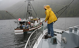 Missionary in rain gear on bow deck of Coastal Messenger.
